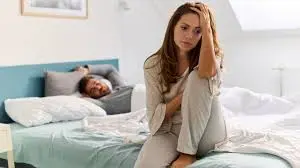 a male and female setting at the bed while the husband is sleeping
